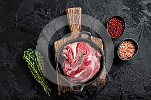 Boneless lamb neck, raw meat in a skillet with herbs. Black background. Top view
