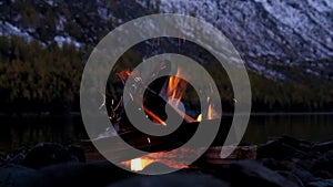 bonfire on the bank of Lower Multinskoe lake in the Altai Mountains at late evening with snow on mountains