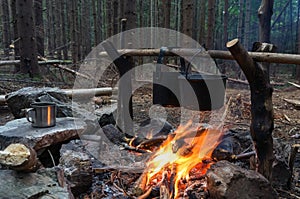 Bonfire at the campers in the evening. Food and tea in two black, smoked pots over the fire. Around the coniferous forest, dusk is