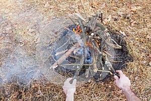 Bonfire in the spring forest on the background of withered grass. In the frame of the hand of a man.