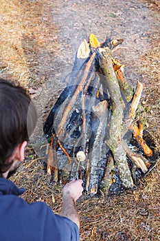 Bonfire in the spring forest on the background of withered grass. In the frame head, shoulder and arm of a man.