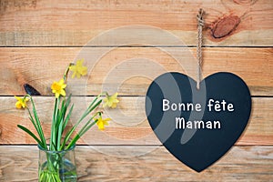 Bonne fete maman, French mothers day card, wood planks with daffodils and a blackboard in shape of a heart