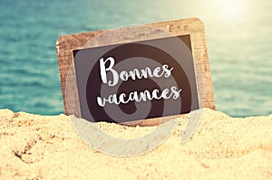 Bonnes vacances meaning Happy holiday in French written on a chalkboard in the sand of a beach