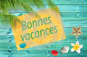 Bonnes vacances (meaning happy summer) written on a paper on colorful wood background with palm trees