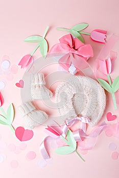 Bonnet and booties on a pink background. Handmade clothes for a newborn, decorative paper flowers. Newborn baby gift concept, mom