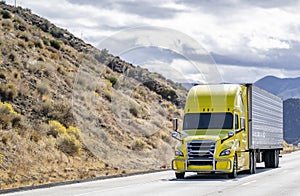 Bonnet bright yellow big rig semi truck tractor transporting frozen cargo in reefer semi trailer climbing uphill on the mountain