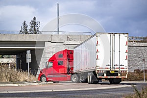 Bonnet red big rig semi truck transporting cargo in dry van semi trailer turning on the round road intersection going under the