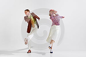 Boogie-woogie. Young man and woman in stylish clothes dancing retro dance against grey studio background