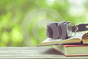 Book and black headphone on wooden table with abstract green nature blur background. Reading and education concept