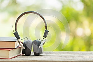 Book and black headphone on wooden table with abstract green nature blur background. Reading and education concept