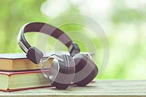 Book and black headphone on wooden table with abstract green nature blur background. Reading and education concept