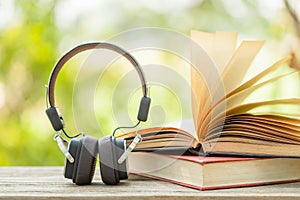 Book and black headphone on wooden table with abstract green nature blur background. Reading and education concept