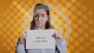 Book club president holds message urging people to join them, studio background