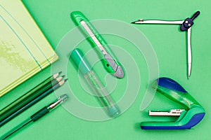 Book, color pencils, pen, felt-tip pen, paper knife, compass and stapler on green background