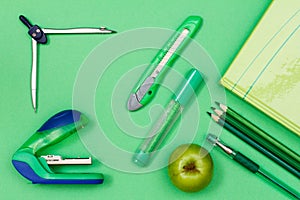 Book, color pencils, pen, felt-tip pen, paper knife, compass and stapler on green background