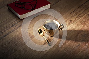 Book and eyeglasses near golden cup of coffee