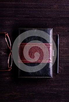 Book, eyeglasses and pen laid on old wooden table