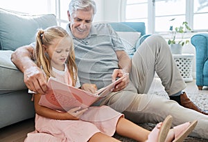 Book, family and children with a girl reading to her grandfather on the floor of their living at home. Kids, read and