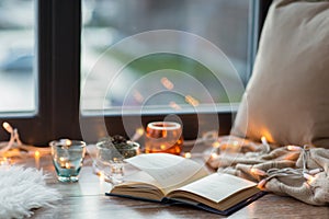 Book, garland lights and candles on window sill