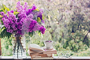 Book, glasses, cup of tea and lilac on a wooden window. Fragrant tea in the garden. Romantic concept