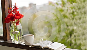 Book, glasses, cup of tea and red tulips on a wooden window. Read and rest.
