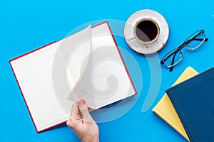 Book in hands for reading and education with coffee and glasses on blue background flatlay