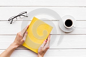 Book in hands for reading and education with coffee and glasses on white wooden background flatlay