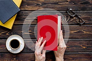 Book in hands for reading and education with coffee and glasses on wooden background flatlay