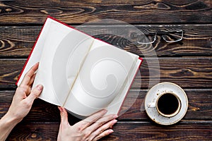 Book in hands for reading and education with coffee and glasses on wooden background flatlay