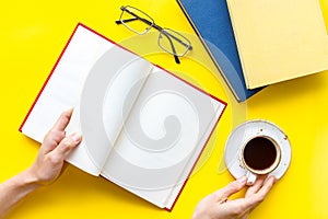 Book in hands for reading and education with coffee and glasses on yellow background flatlay