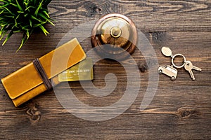 Book a hotel. Hotel service bell, bank card and room keys on dark wooden table background top view copyspace