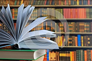 Book in library with old open textbook, stack piles of literature text archive on reading desk, and aisle of bookshelves in school