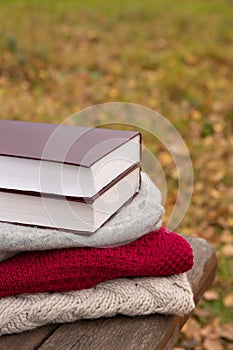 Book lies on knitted sweater on rough boards of wooden bench in park. Autumn background or postcard