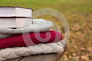 Book lies on knitted sweater on rough boards of wooden bench in park. Autumn background or postcard