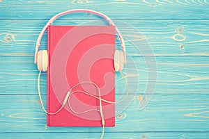 Book and new modern pink music headphone on blue wooden plank ba