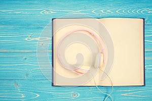 Book and new modern pink music headphone on blue wooden plank ba