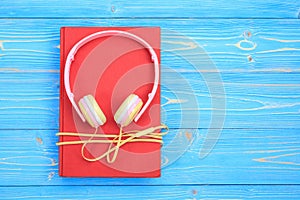 Book and new modern pink music headphone on blue wooden plank ba