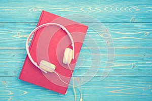 Book and new modern pink music headphone on blue wooden plank ba