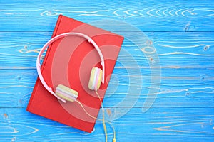 Book and new modern pink music headphone on blue wooden plank ba