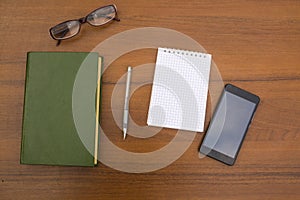 Book, notepad, pen, eyeglasses and smart phone on wooden desk