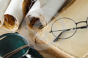 A book with old-fashioned glasses, a magnifying glass and rolled up old parchments