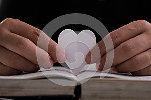 Book with open pages and heart shaped paper. Woman hand holding heart shaped paper over open book on table. love of reading
