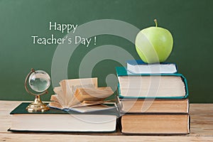 Book pile with apple, globe, pencils and sharpener on the school blackboard. Teacher`s day concept