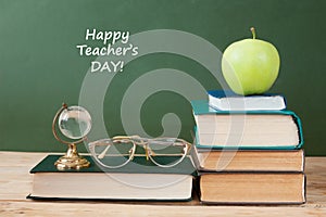 Book pile with apple, globe, pencils and sharpener on the school blackboard. Teacher`s day concept