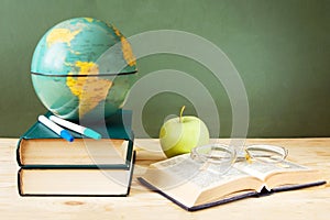 Book pile with apple, globe, pencils and sharpener on the school blackboard. Teacher`s day concept