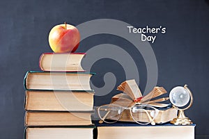 Book pile with apple, globe, pencils and sharpener on the school blackboard. Teacher`s day concept