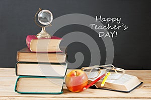 Book pile with apple, globe, pencils and sharpener on the school blackboard. Teacher`s day concept