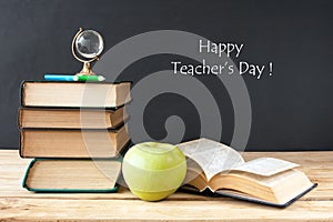 Book pile with apple, globe, pencils and sharpener on the school blackboard. Teacher`s day concept