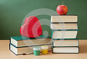 Book pile with apple, globe, pencils and sharpener on the school blackboard. Teacher`s day concept