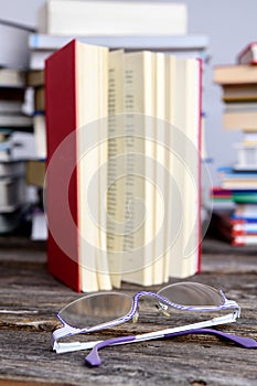 Book and reading glasses in front of piles of different books